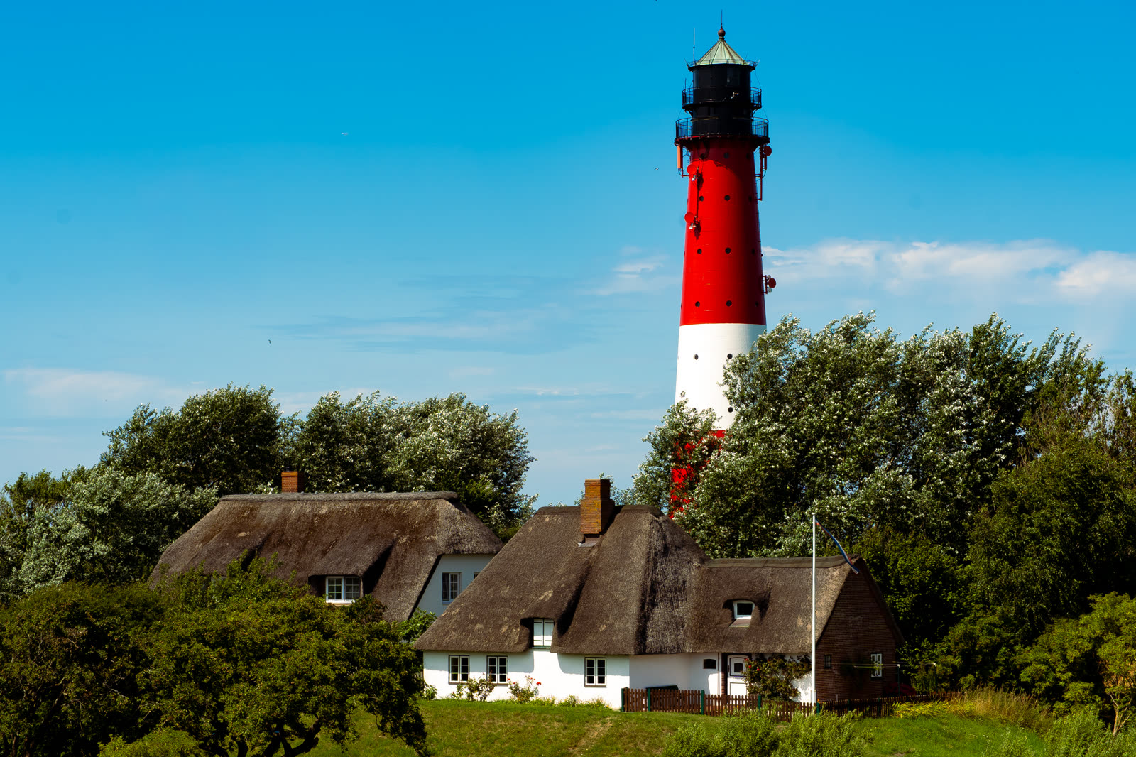 Leuchtturm hinter Reetdachhäusern — Landschaftsfotografie von Martina Ziegler